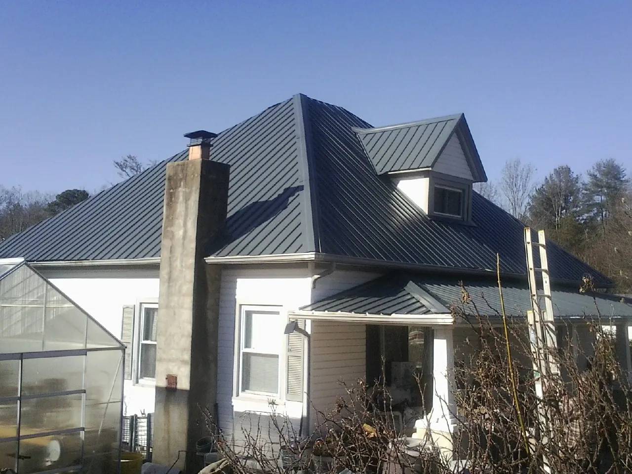 Dark blue standing seam metal roof on a white farmhouse with dormer — Slate & Tile Roof Repair by Roofing Brothers in Payne