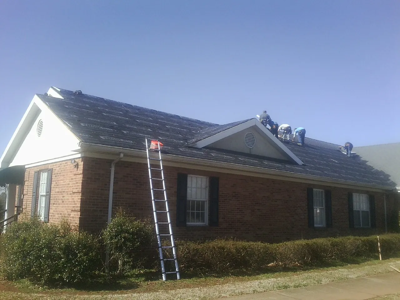 Crew tearing shingles off a brick ranch roof with a ladder set — Emergency Roof Repair work by our crew in Payne