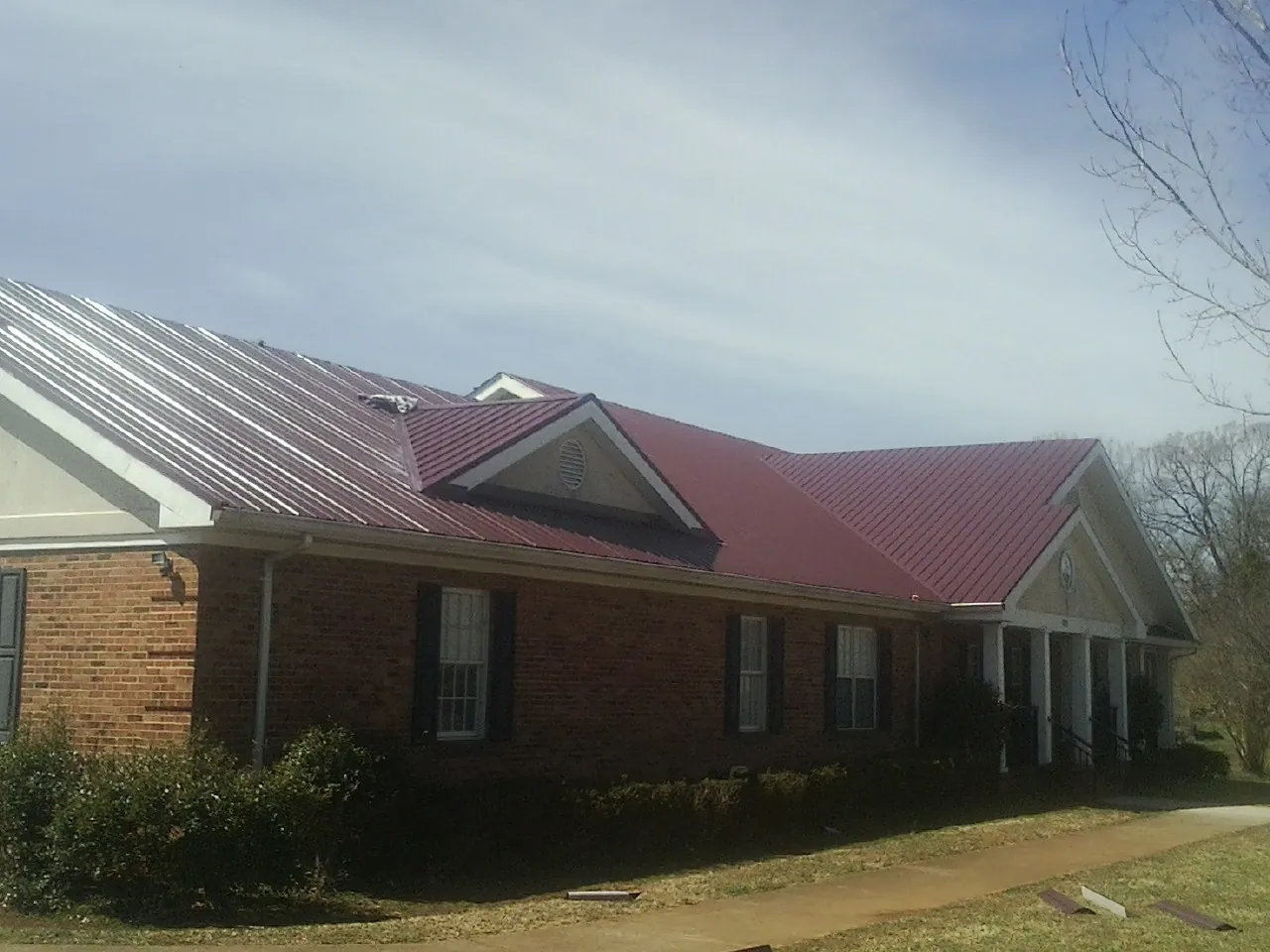 Red metal roof with gabled entries on a long brick building, from a Hail Damage Roof Repair job in Payne