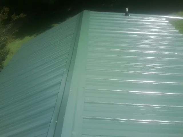 New green metal panels meeting at the ridge of a roof — Flat Roof Repair work by our crew in Payne