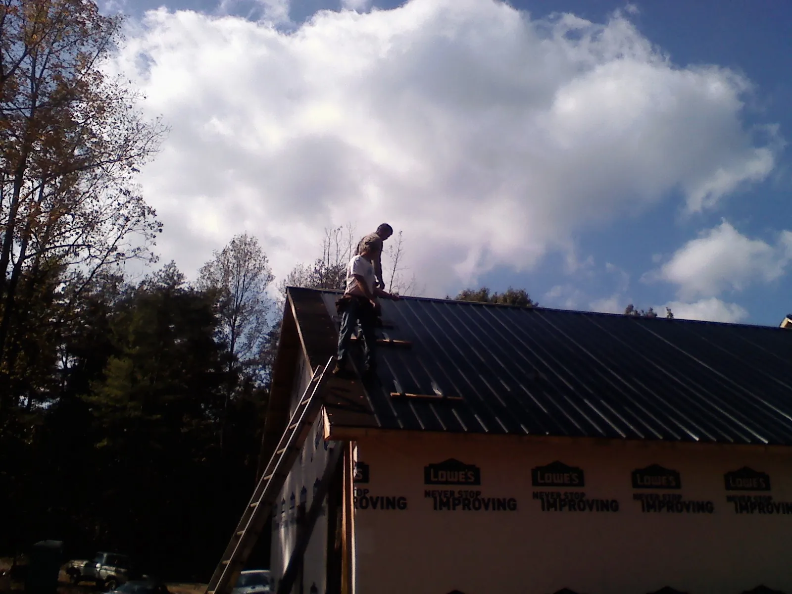 Roofer fastening dark metal panels high against a cloudy sky, from a Roof Inspection job in Payne