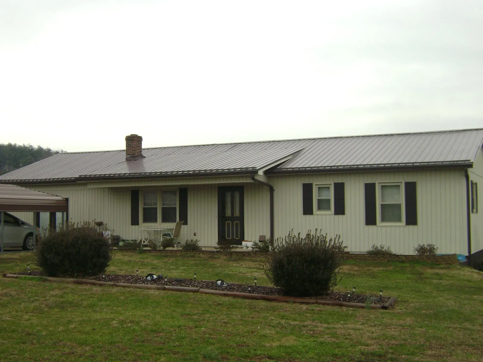 Brown metal roof on a cream sided ranch home with a brick chimney in Payne
