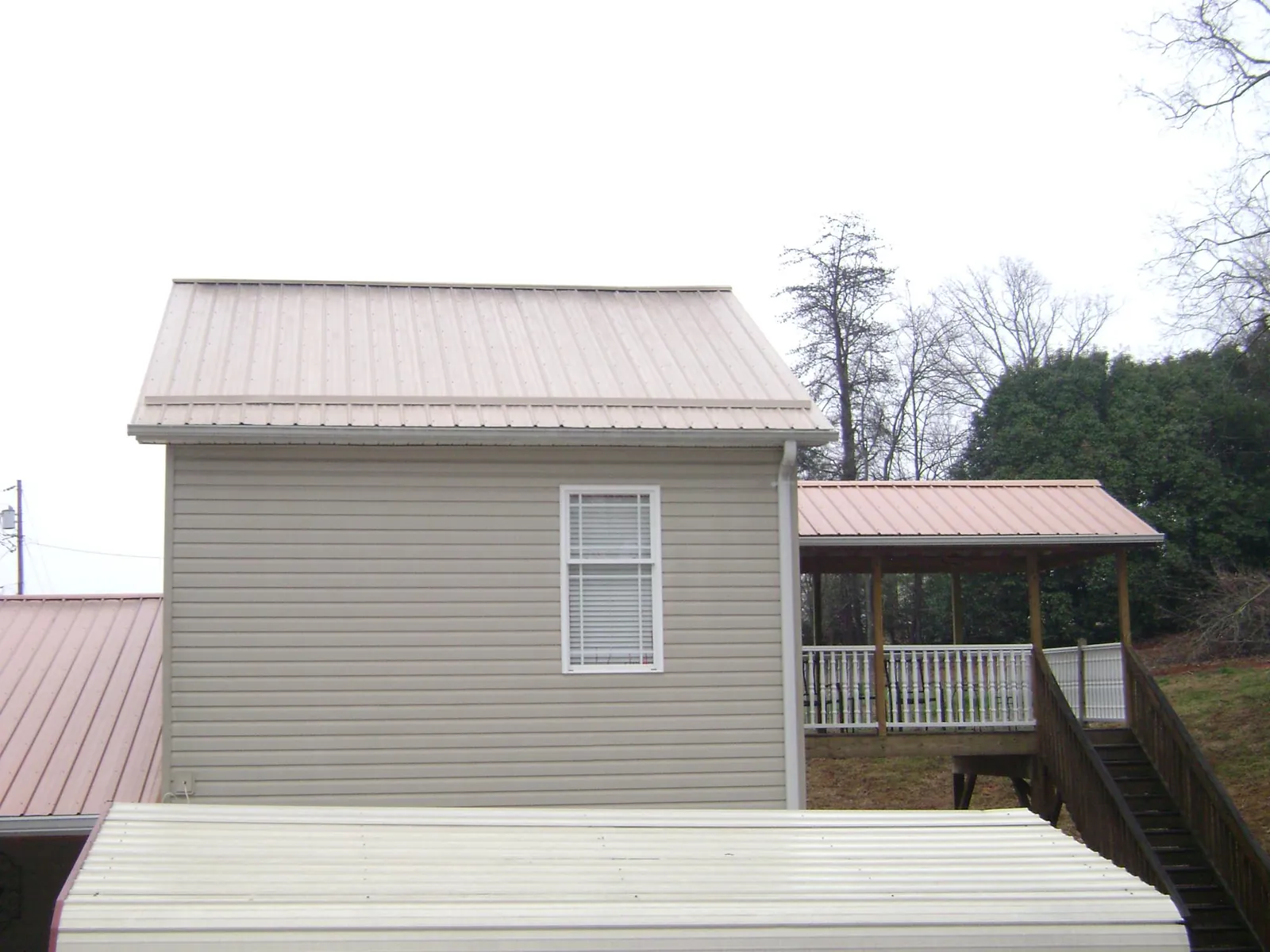 Tan metal roofs on a two story addition and attached porch, from a Roof Replacement job in Payne